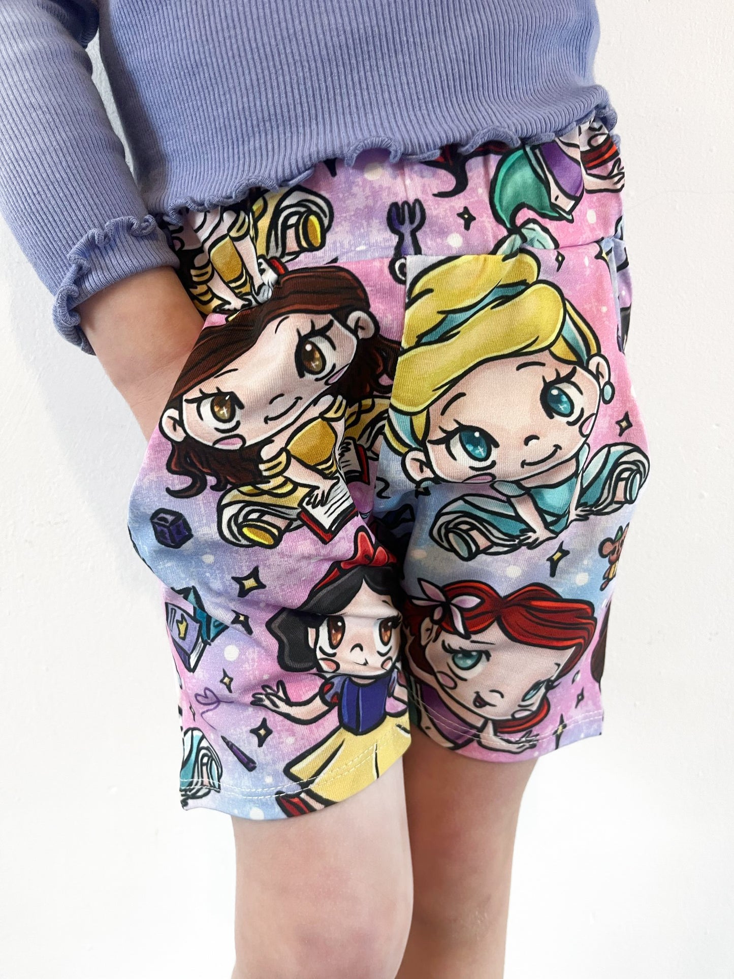 Child wearing pastel jogger shorts with kawaii princess characters, stars and magical background